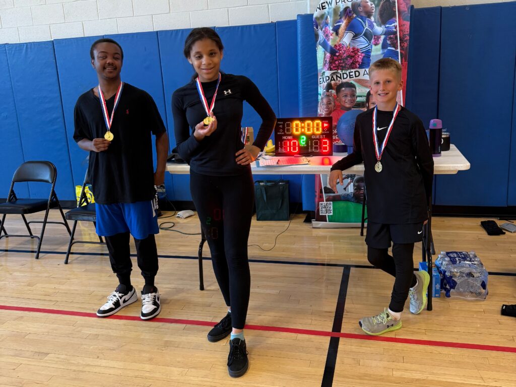 ZaNyiah and her teammates on the Eagles are dressed in their team color black and pose with their gold medals in front of the scoreboard displaying the final score (10-3) of the championship game of MWABA's Youth Goalball Tournament held in June.