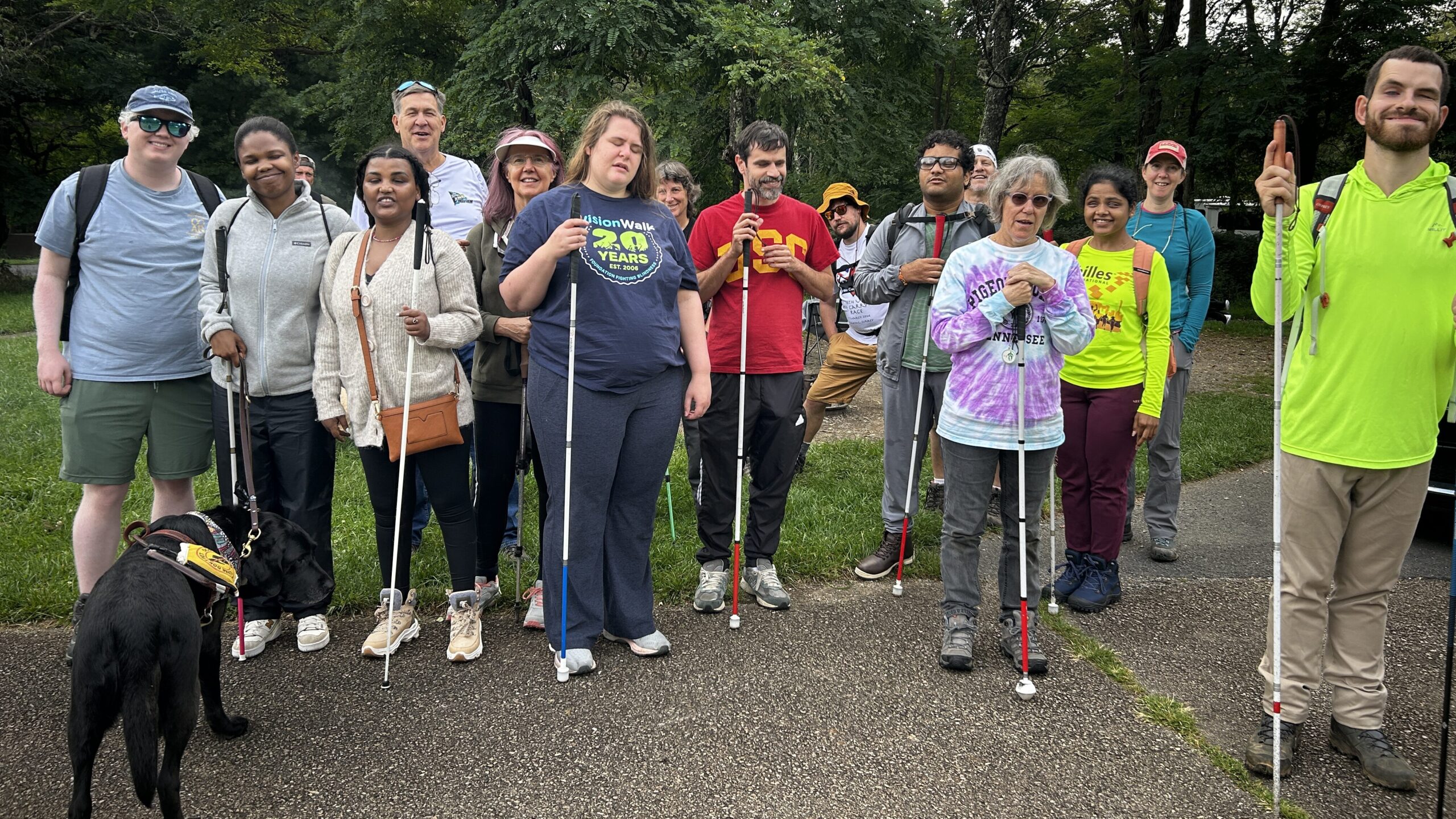 Quincy, Lizzy (with her dog), Dave, Sam, Bill, Carol, Caroline, Sharon, Marcos, Tyler, Maitreya, Brian, Mary, Divya, Rachel, and Kevin standing and smiling, ready to leave the Big Meadows campground for the hike in Shenandoah.